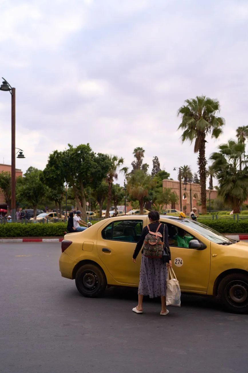 Voyageuse montant dans un petit taxi de Marrakech devant les remparts ocre de la ville
