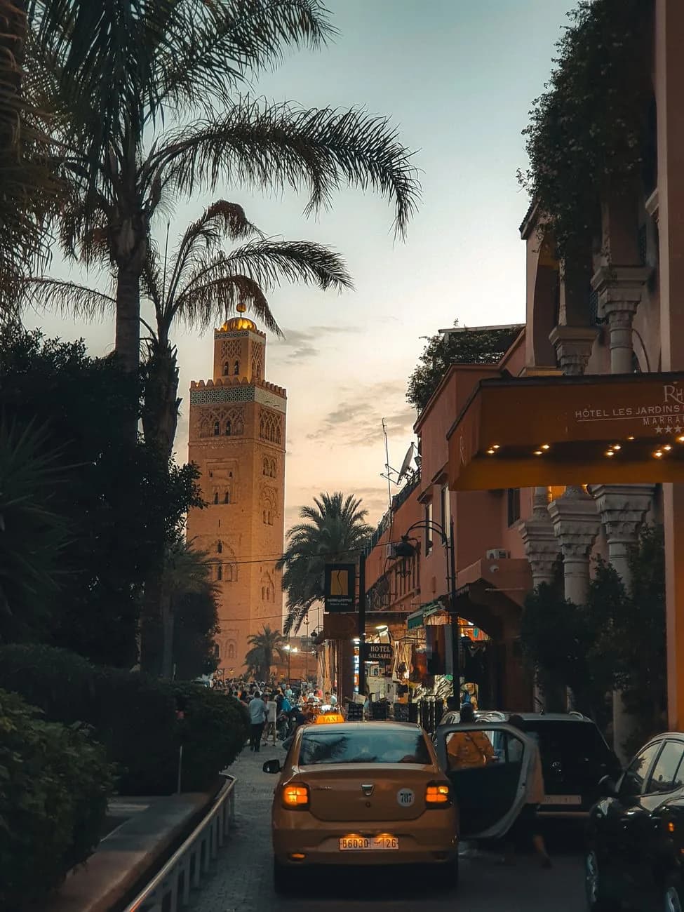 Petits taxis beiges de Marrakech dans une rue menant au minaret de la Koutoubia au crépuscule