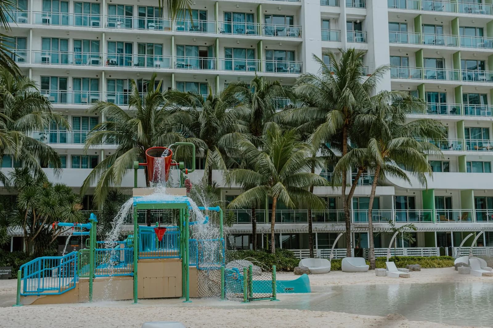 Aire de jeux aquatique pour enfants avec seau basculant et petits toboggans devant les bâtiments d'un resort