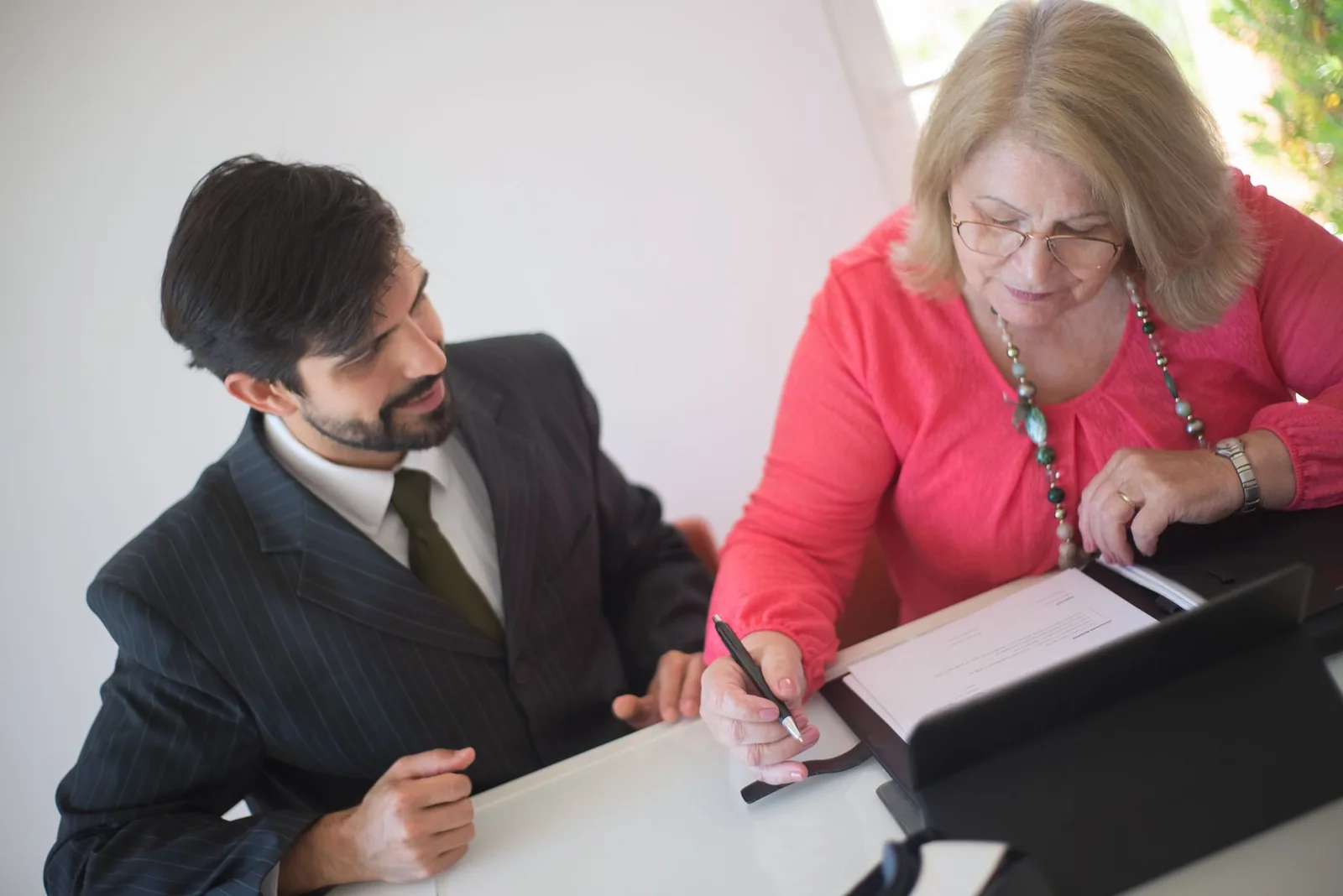 Rendez-vous avec un conseiller en costume : une cliente en rose signe un document posé sur la table