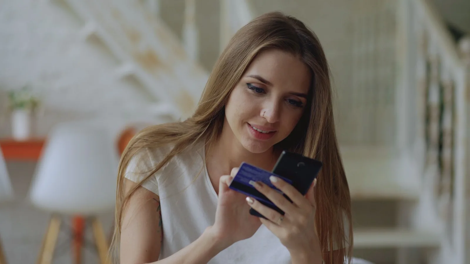 Jeune femme qui tient une carte bancaire et un smartphone pour effectuer un virement depuis son salon