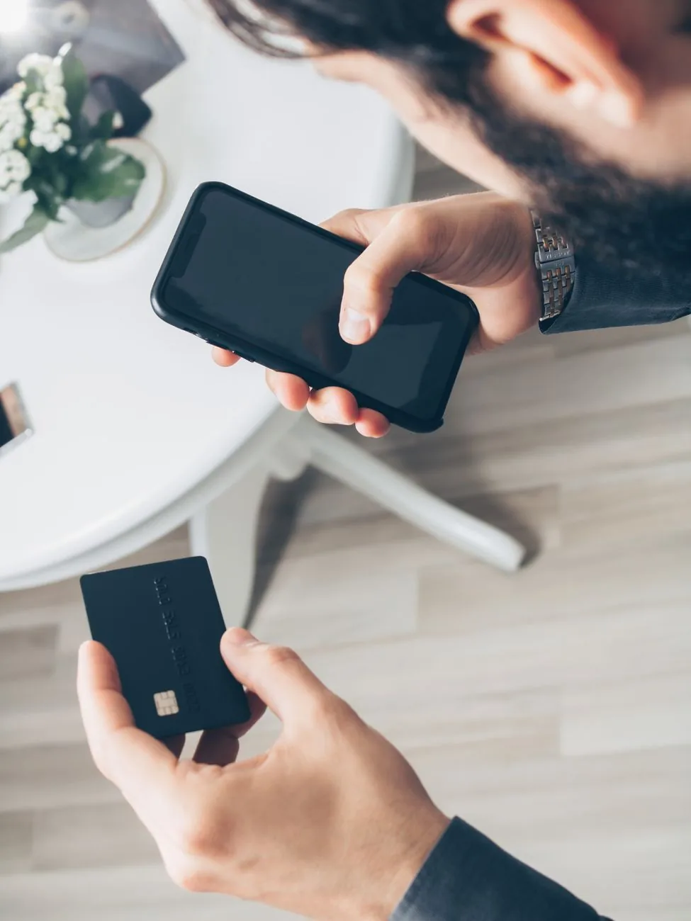 Homme vu du dessus, un smartphone dans une main et une carte bancaire dans l'autre, à une table