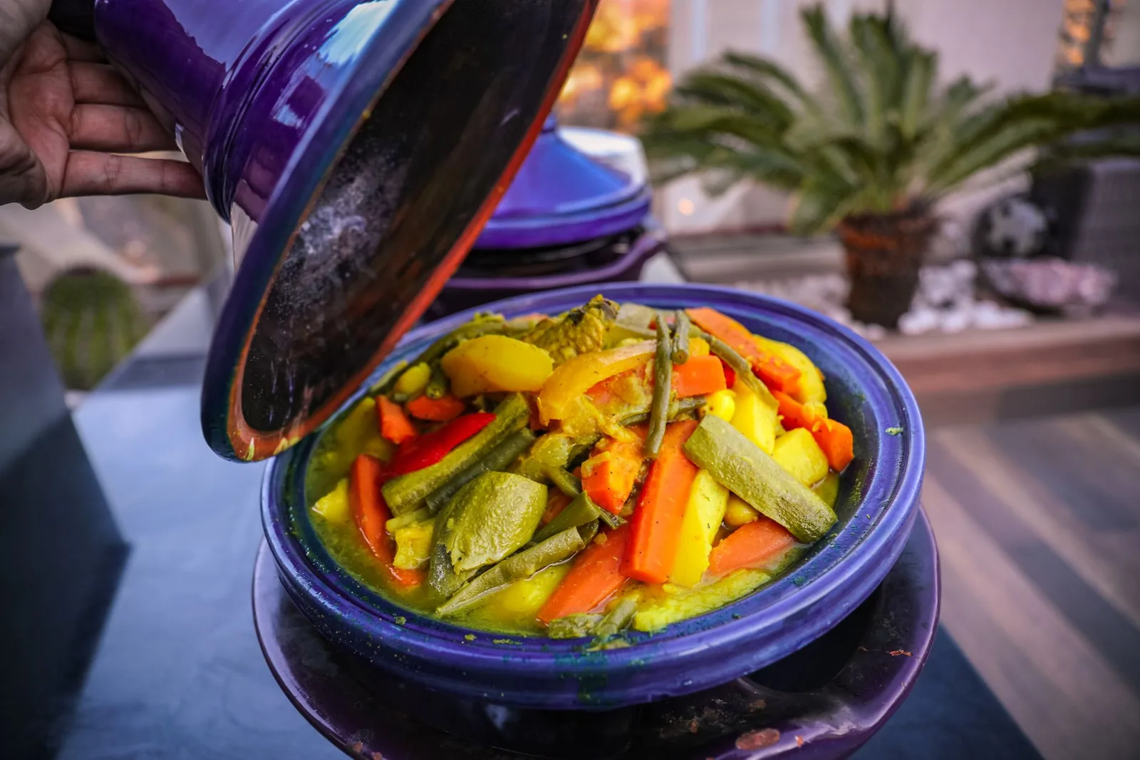 Tajine de légumes marocain dans son plat en terre violet, couvercle soulevé