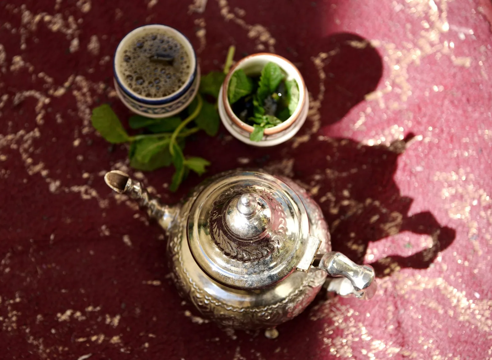 Théière en argent, verres à thé et bouquet de menthe fraîche sur un tapis marocain