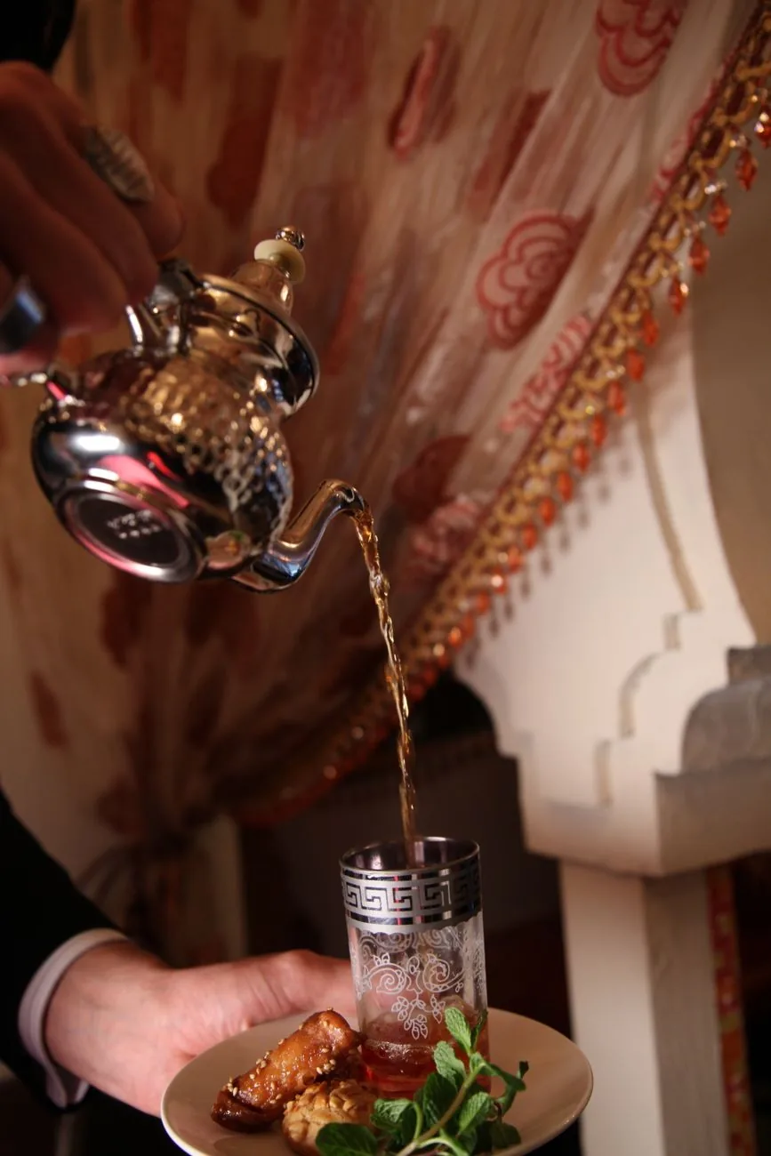 Thé à la menthe versé de haut dans un verre gravé, avec des pâtisseries marocaines, dans un riad
