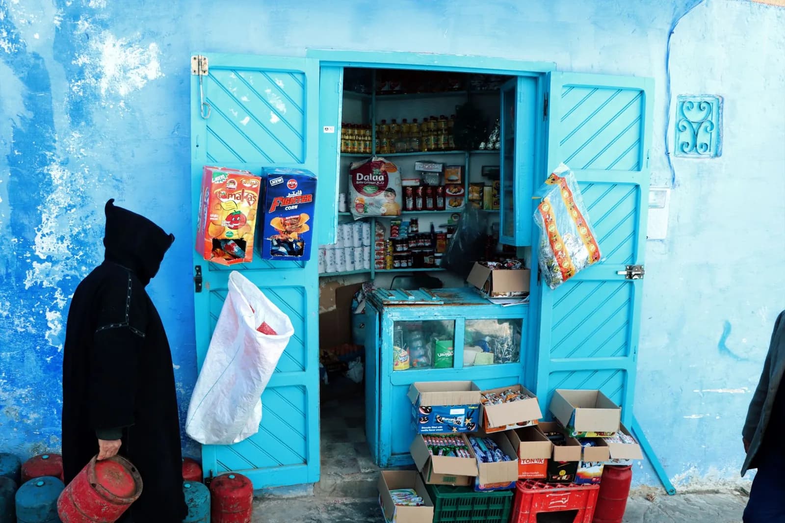 Petite épicerie de rue aux portes bleues, avec paquets de biscuits et bonbons exposés, au Maroc