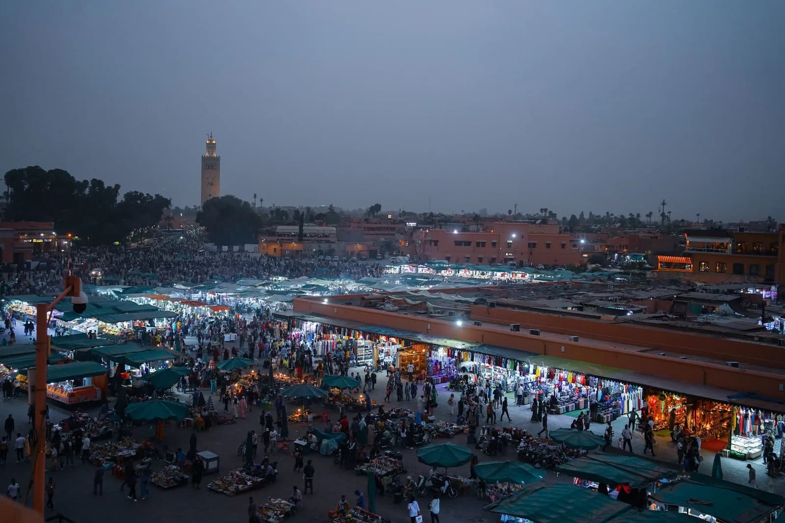 Place Jemaa el-Fna à Marrakech au crépuscule, vue en hauteur sur les stands éclairés, la foule et le minaret de la Koutoubia