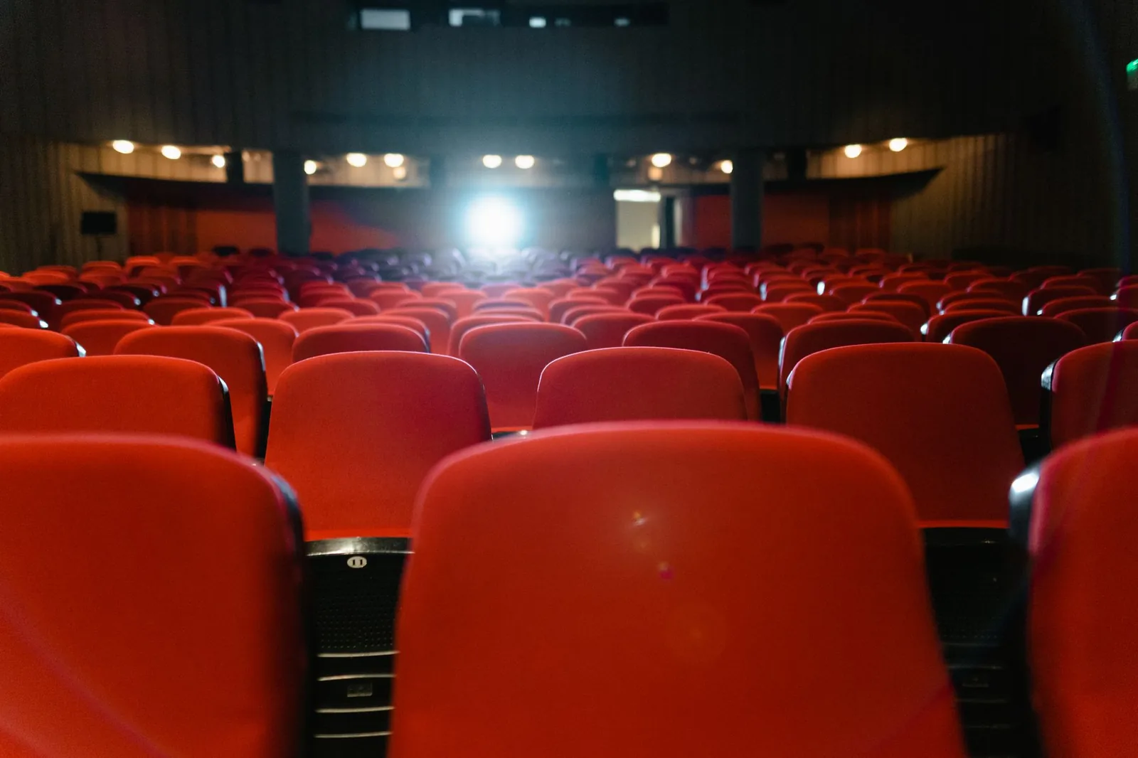 Salle de cinéma vue depuis les rangées de sièges rouges, avec le faisceau lumineux du projecteur au fond