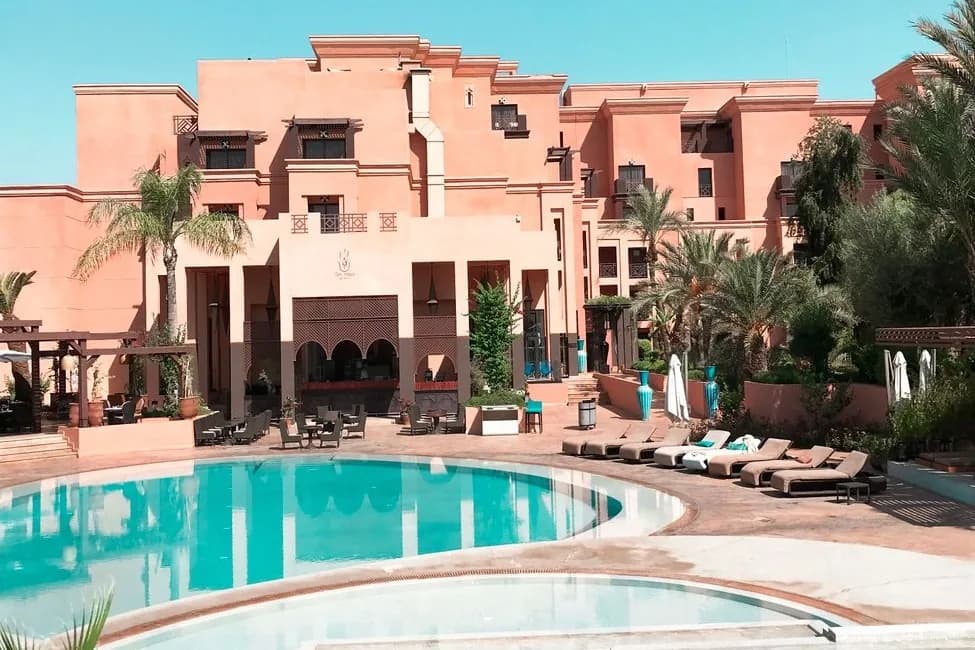 Piscine d'un hôtel-club devant une façade ocre de style marocain, avec transats et palmiers