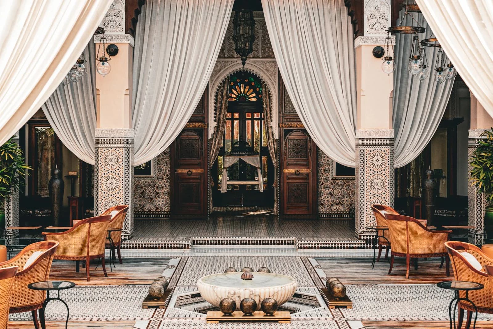 Patio d'un riad traditionnel à Marrakech avec fontaine en marbre, arcades sculptées et zellige