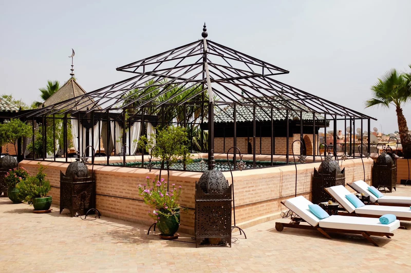 Terrasse sur le toit d'un riad à Marrakech avec transats, lanternes marocaines et palmier
