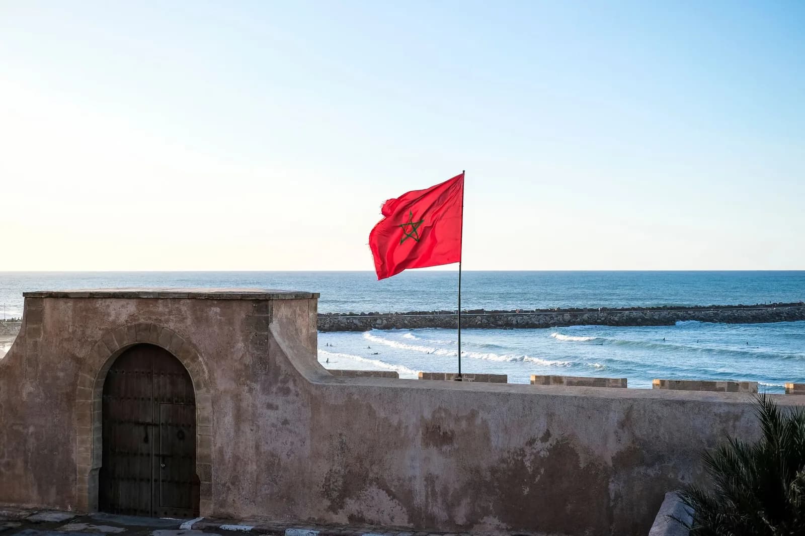 Drapeau marocain rouge à étoile verte flottant au-dessus d'un rempart en pierre face à l'océan