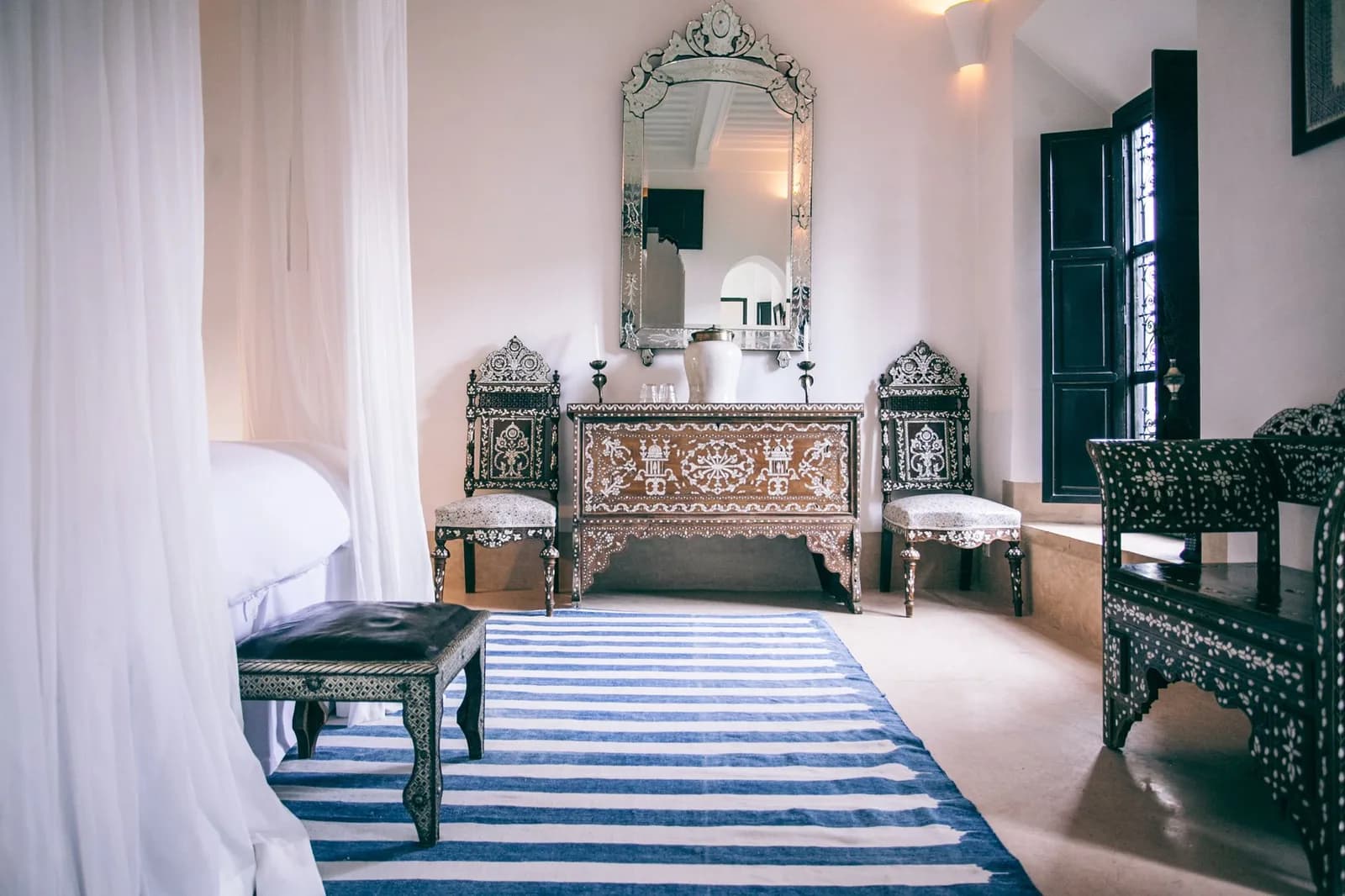 Chambre de style marocain avec miroir ouvragé, mobilier incrusté et grands rideaux blancs