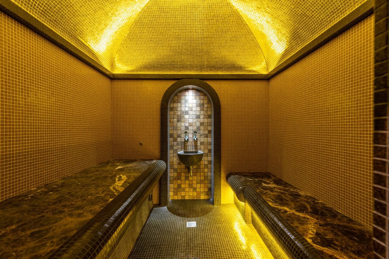 Hammam à mosaïque dorée et banquettes de marbre dans un spa de style marocain