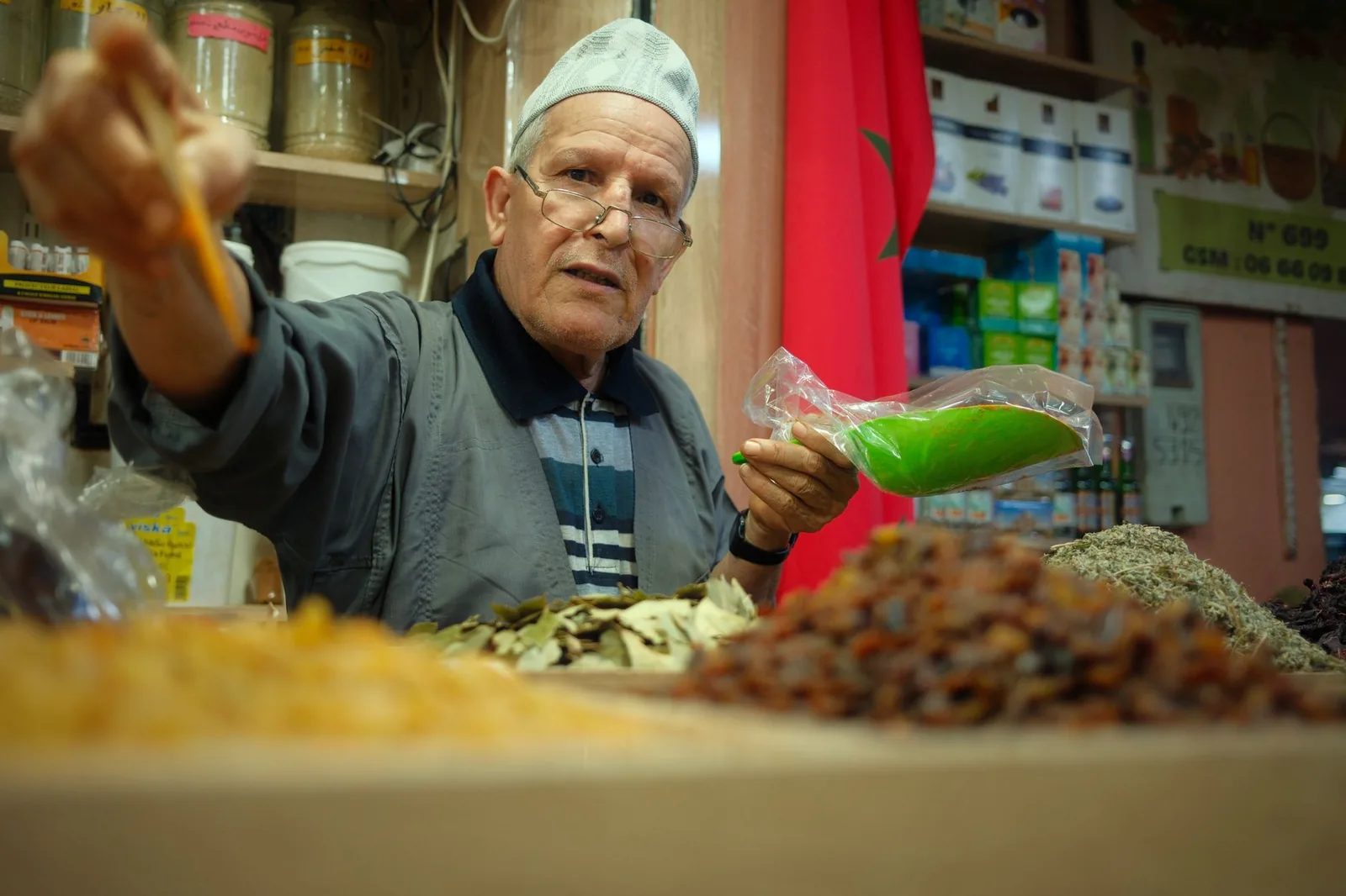 Marchand d'épices dans un souk de Marrakech tendant un sachet par-dessus son étal