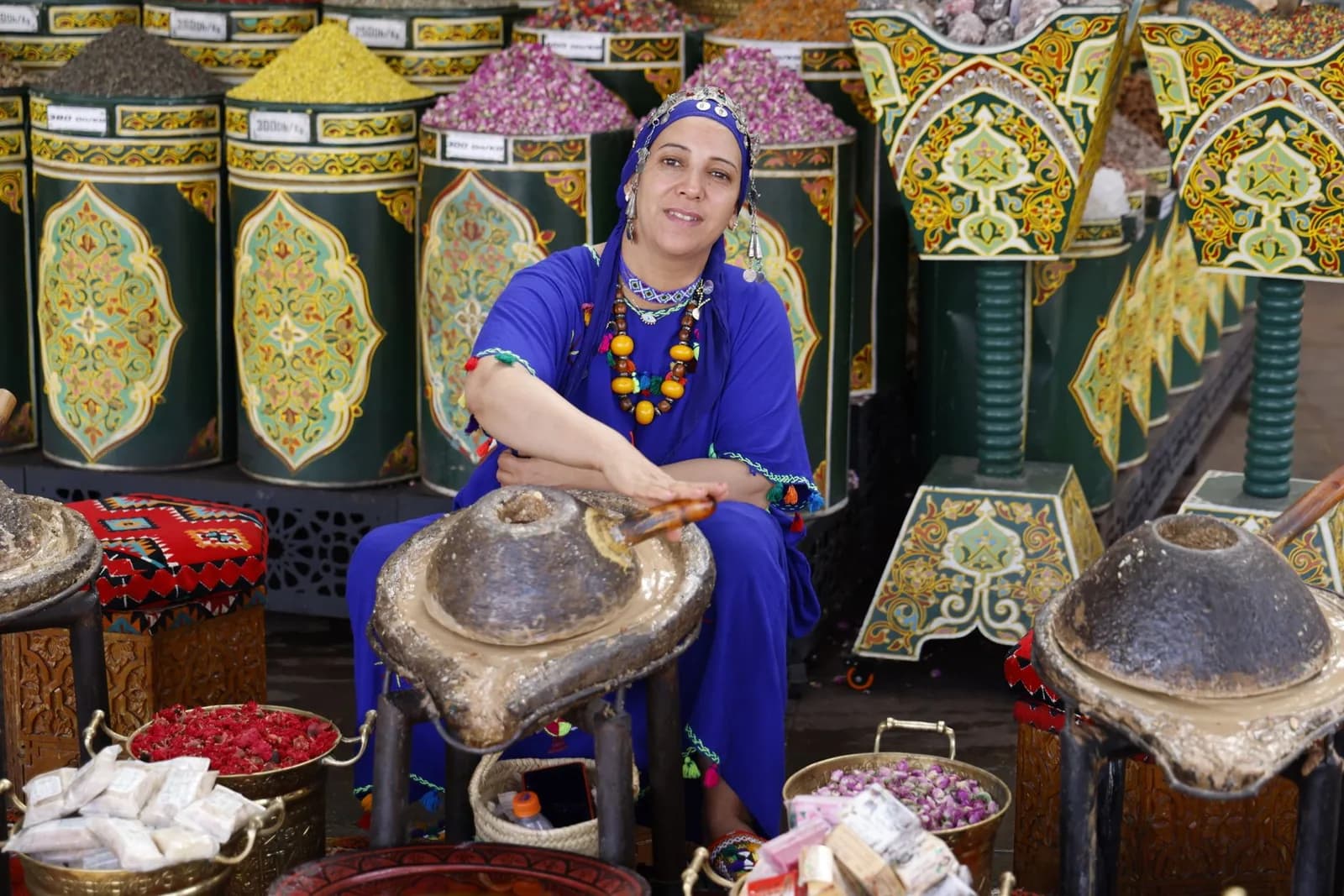 Vendeuse d'épices et de plantes assise derrière ses bocaux étiquetés dans le souk de Marrakech