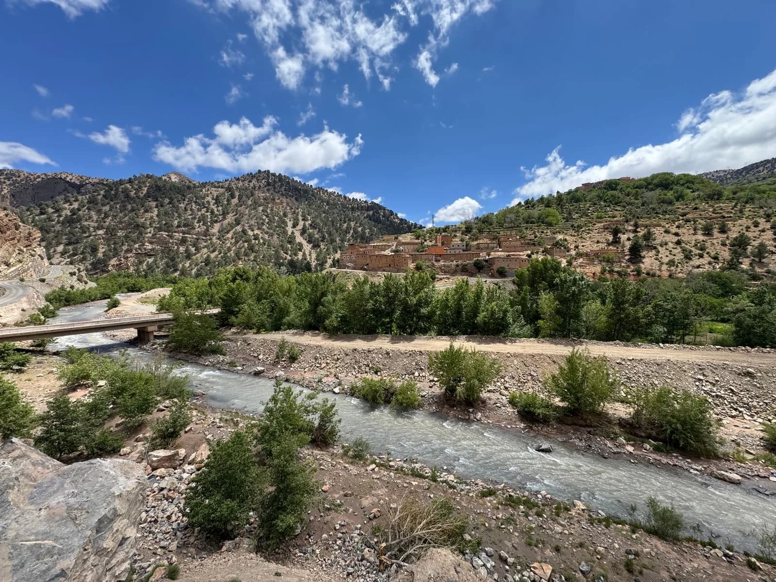 Rivière au fond d'une vallée de montagne, avec un pont et un village de maisons en terre sur le versant
