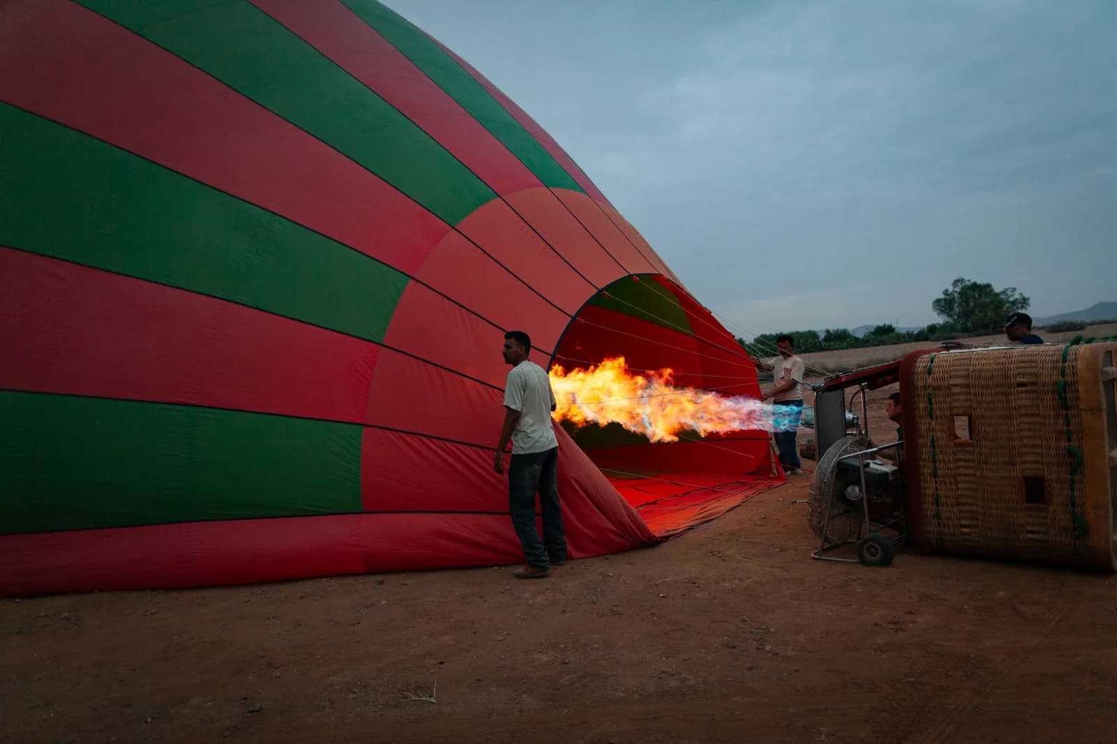 Gonflage d'une montgolfière rouge et verte au brûleur, flamme orangée, à l'aube près de Marrakech