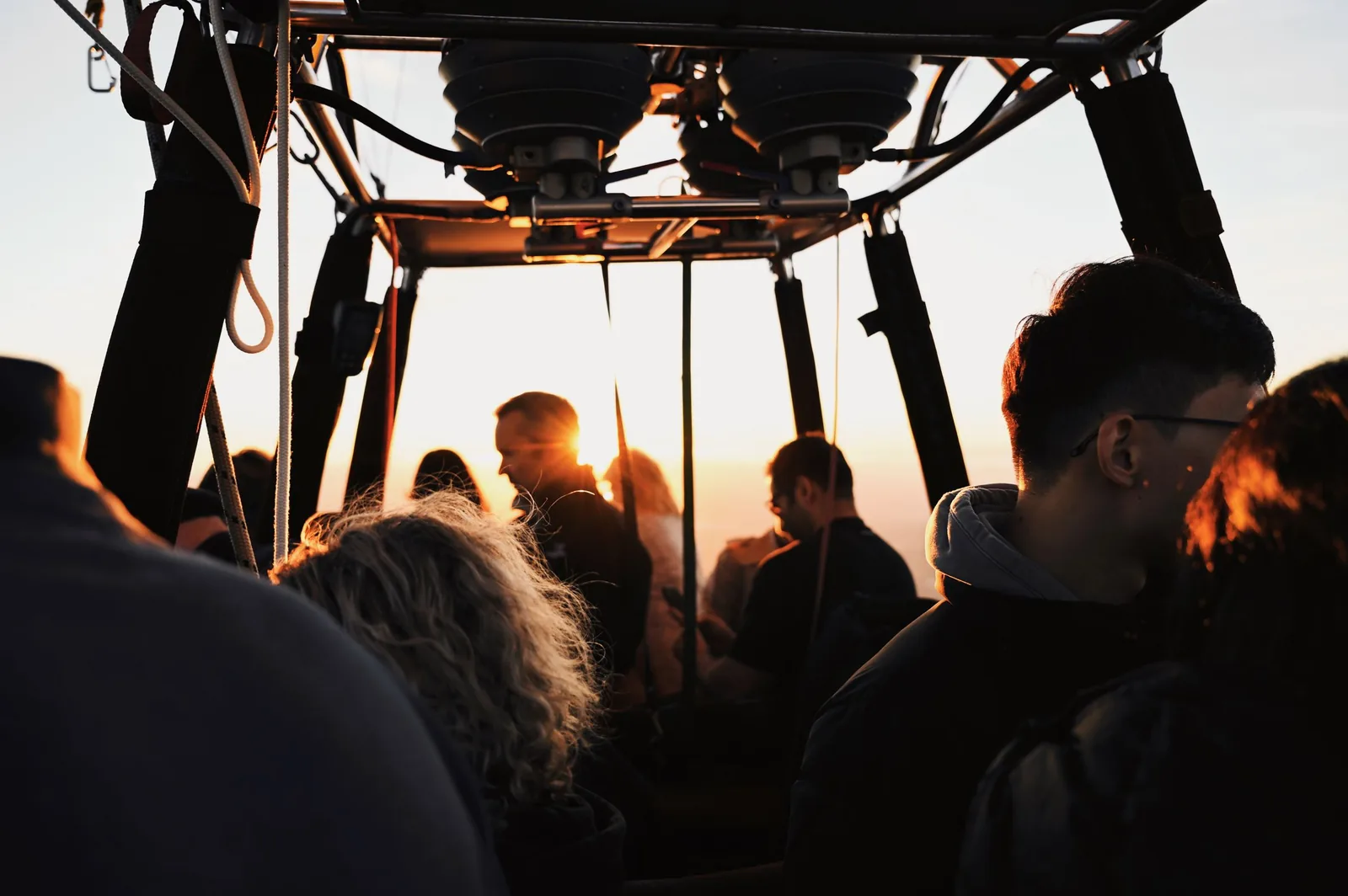 Passagers debout dans la nacelle d'une montgolfière, en contre-jour devant le soleil bas