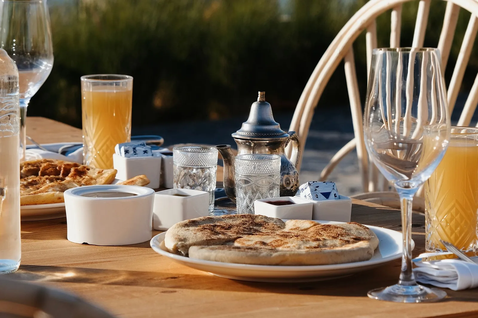 Petit-déjeuner en extérieur près de Marrakech : galette de pain, théière argentée, jus d'orange et petits pots sur une table en bois