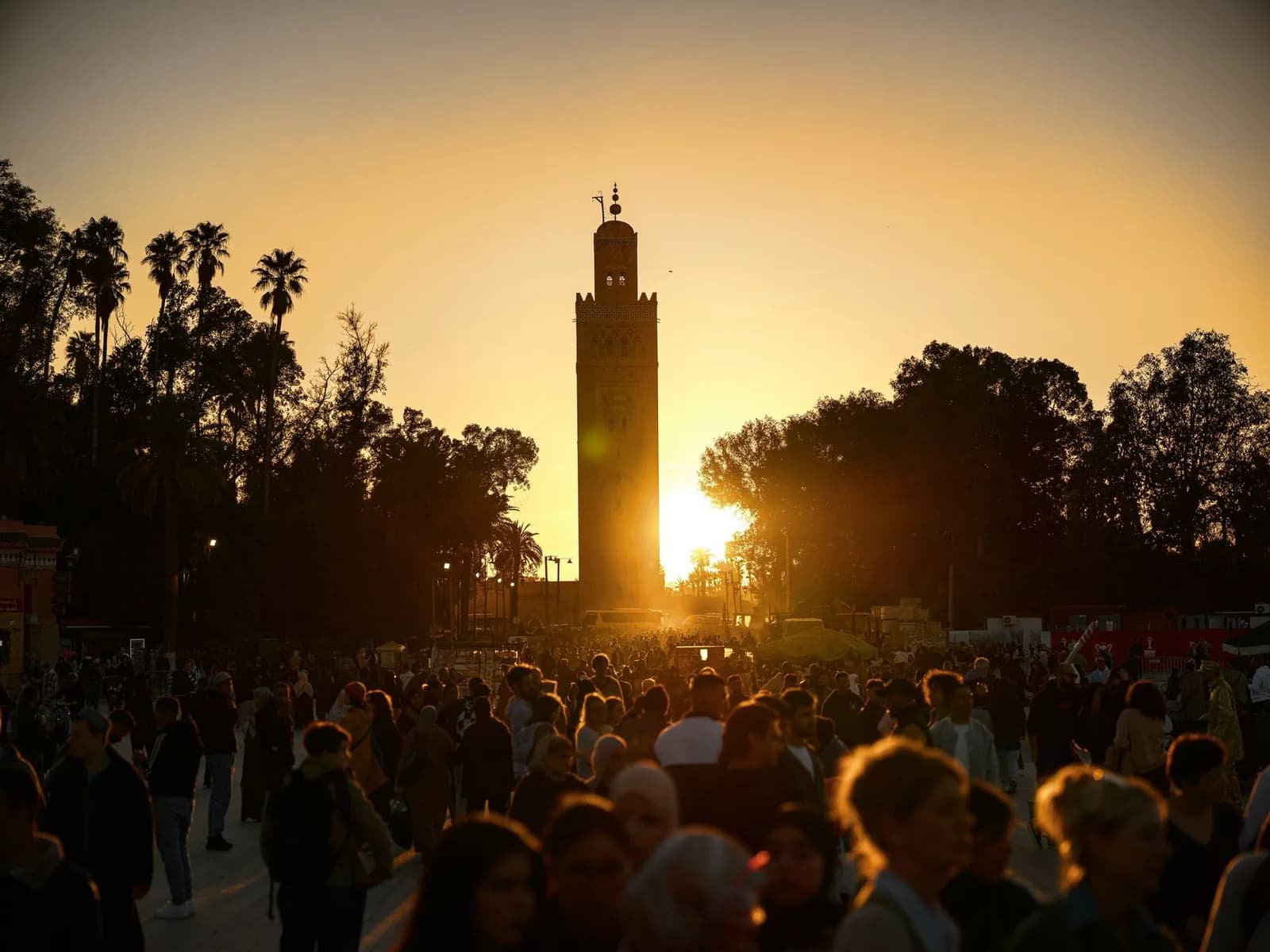 Le minaret de la mosquée Koutoubia à contre-jour au coucher du soleil, au-dessus de la foule de la place Jemaa el-Fna à Marrakech