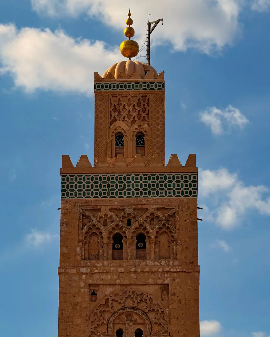 Le sommet du minaret de la Koutoubia à Marrakech, sa lanterne, sa frise de céramique verte et les boules dorées du jamour