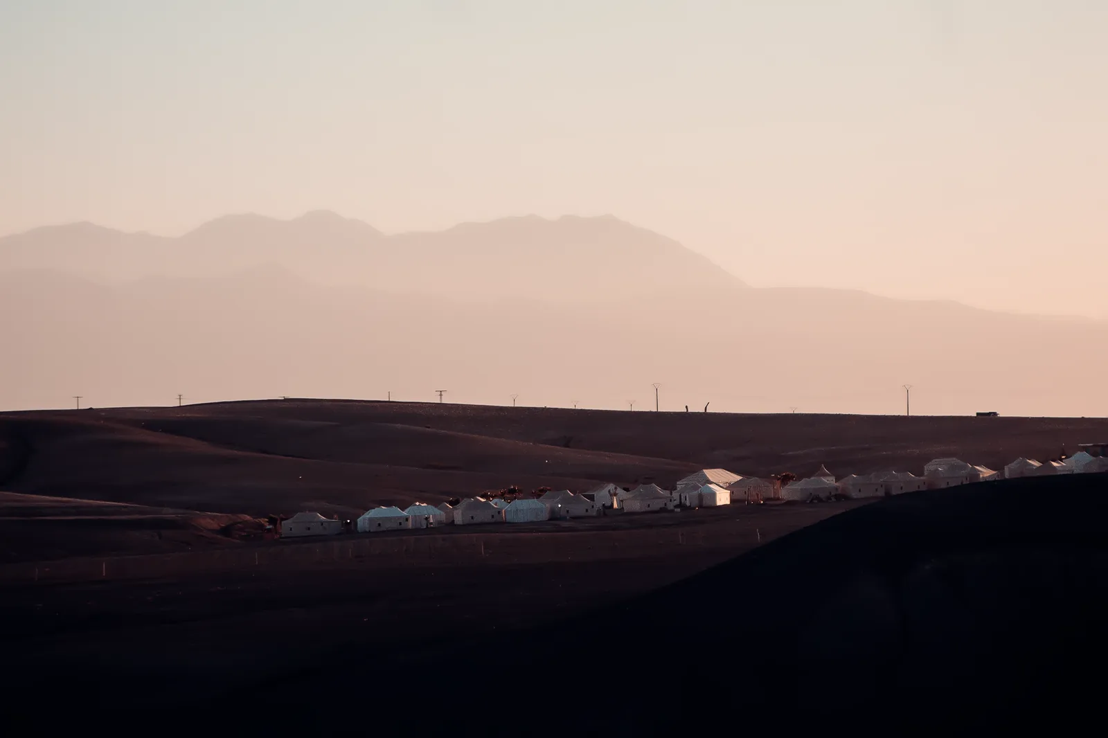 Rangée de tentes d'un camp dans le désert d'Agafay au crépuscule, avec les montagnes de l'Atlas en arrière-plan