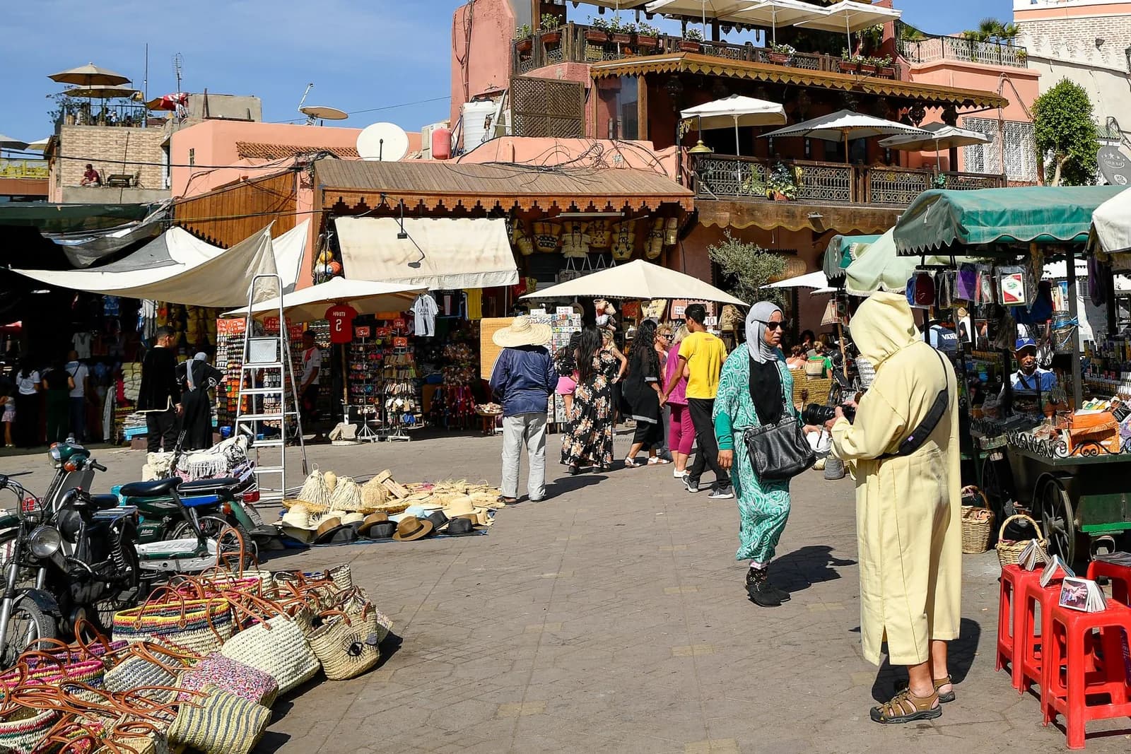 Étals et passants en djellaba sur la place Jemaa el-Fna, sous le soleil d'hiver à Marrakech