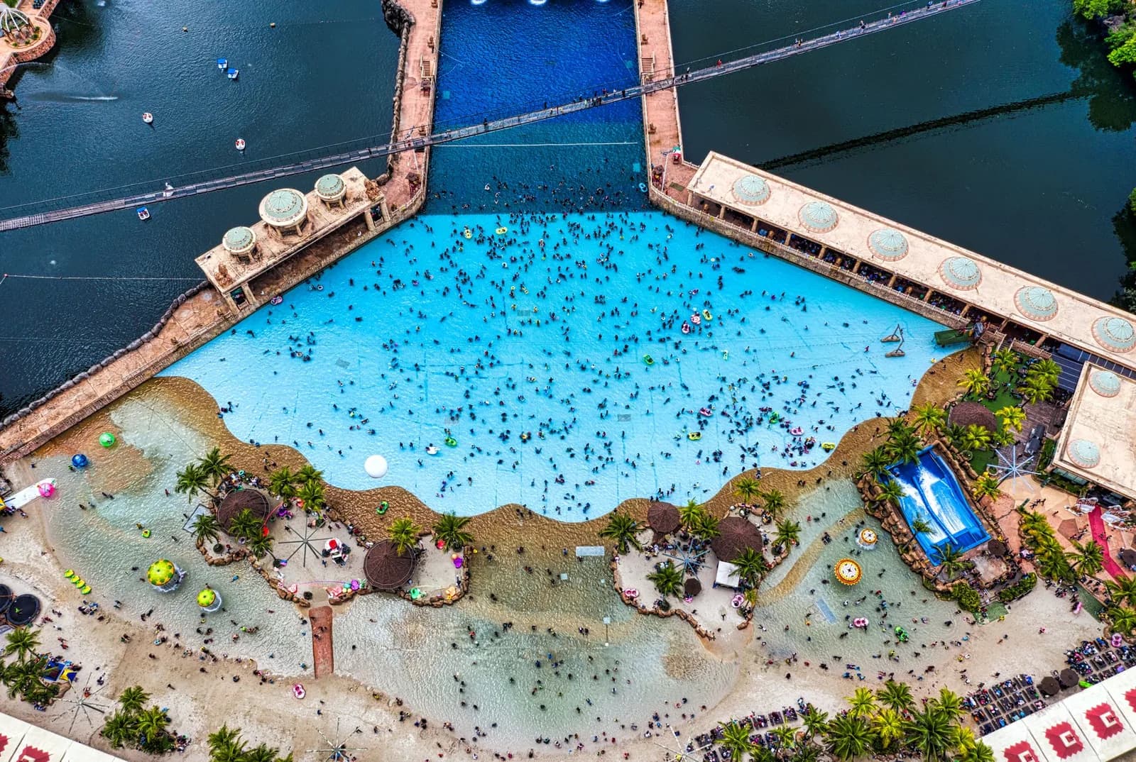 Vue aérienne d'une piscine à vagues de parc aquatique bordée d'une plage artificielle et de palmiers
