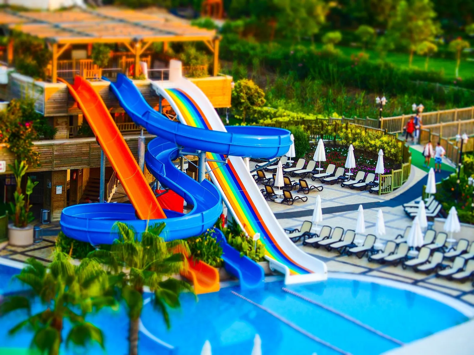 Toboggans colorés d'un parc aquatique entourés de palmiers, de jardins et de transats