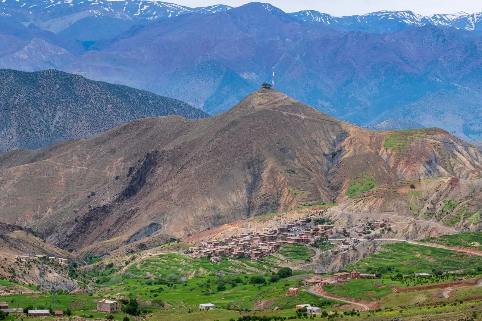 Village de montagne et terrasses vertes dans le Haut Atlas au printemps, sommets encore enneigés au loin