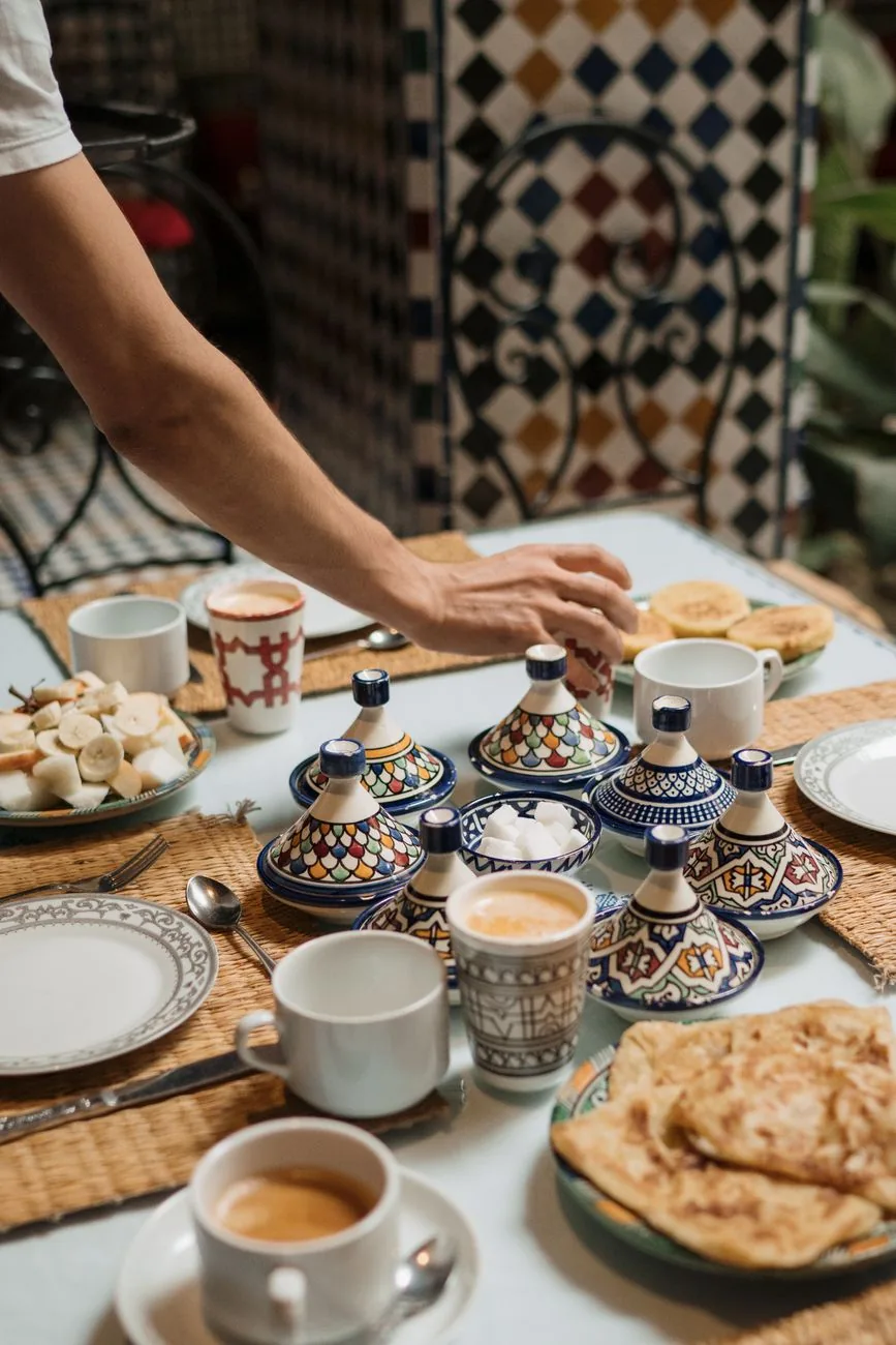 Table de petit déjeuner marocain avec msemen, tagines à épices, café et verres à thé décorés