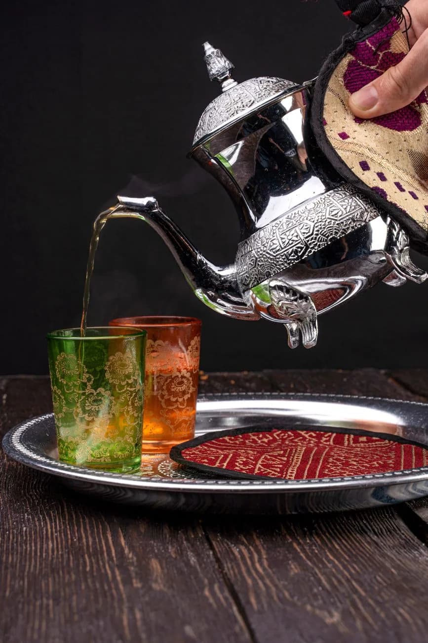 Thé à la menthe marocain versé de haut depuis une théière en argent dans des verres décorés