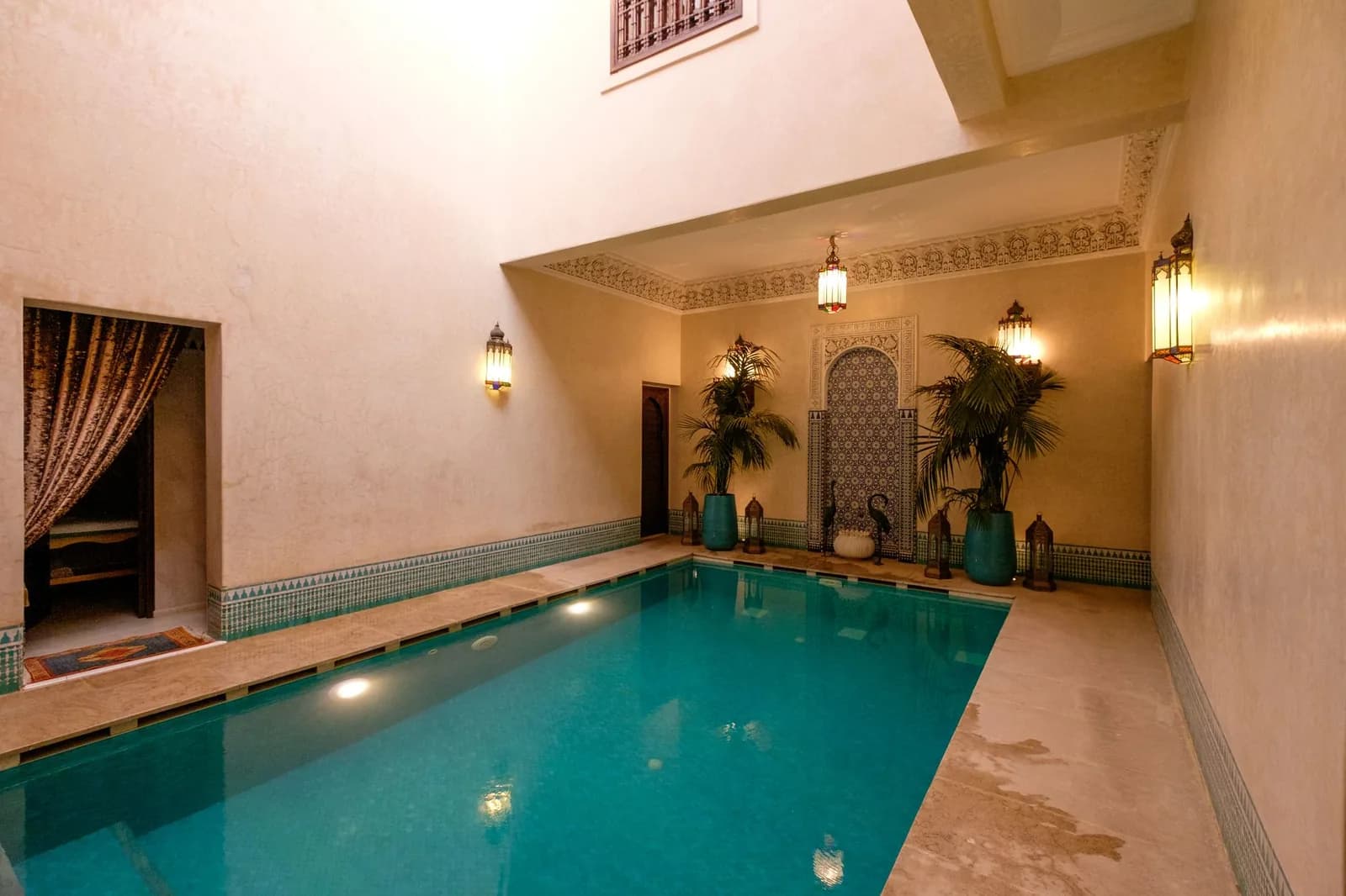 Piscine turquoise d'un hôtel marocain à Marrakech, entourée de murs ocre et de palmiers