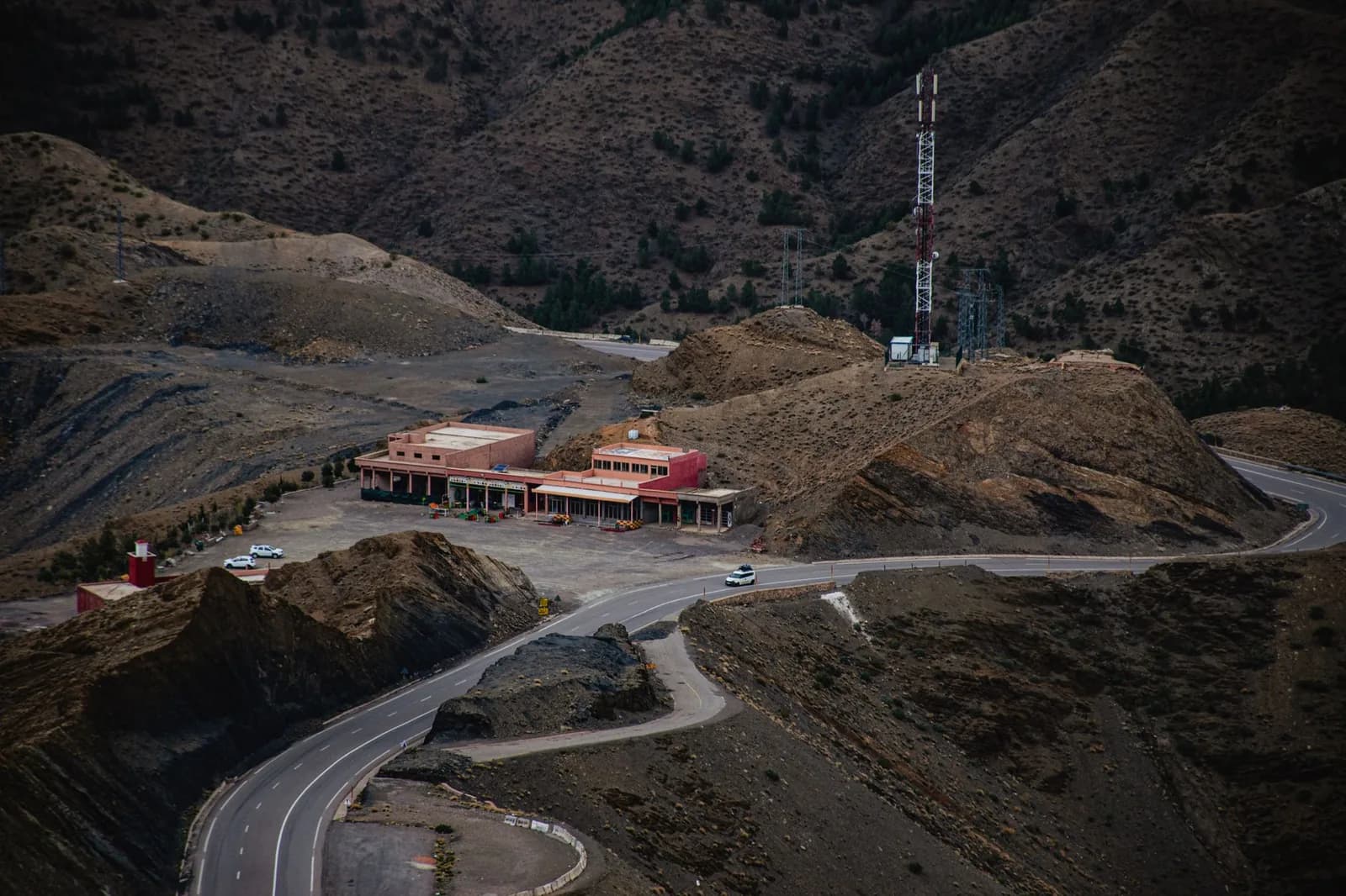 Route sinueuse du Haut Atlas marocain passant devant une halte routière et un relais télécom
