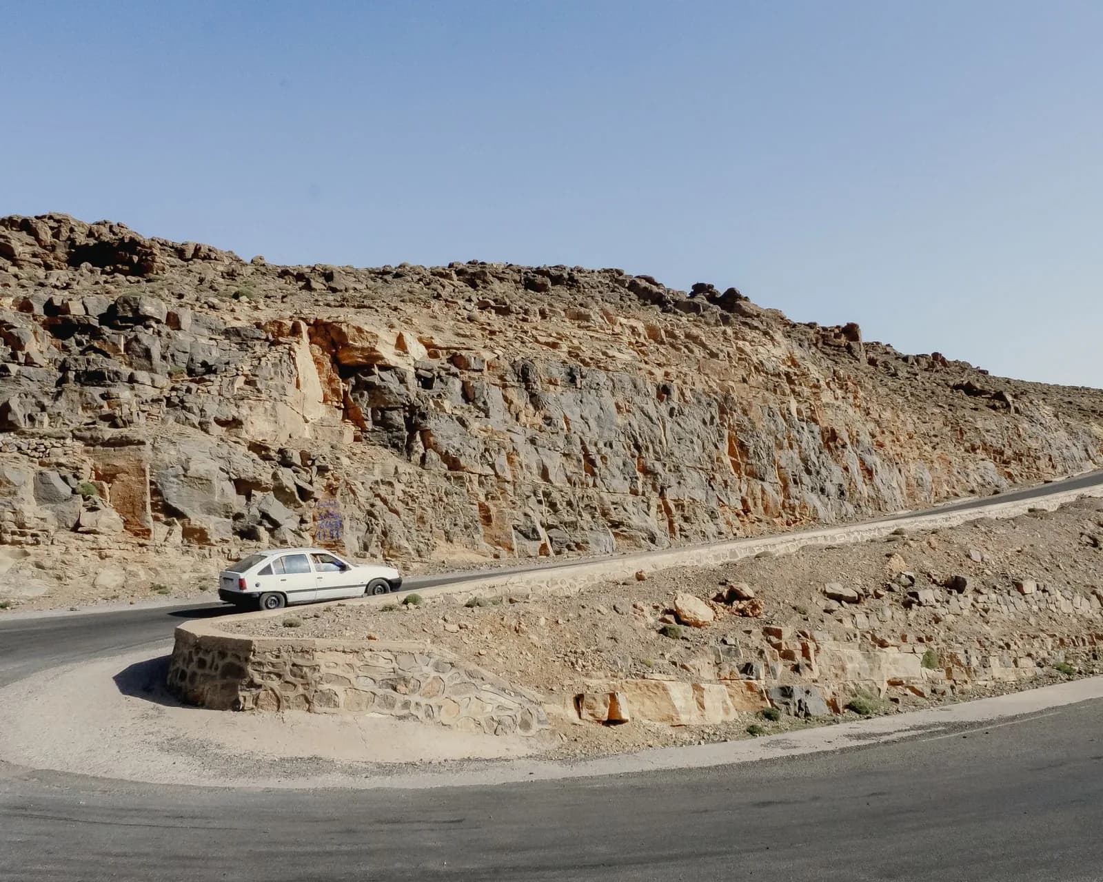 Voiture blanche dans un virage en lacet sur une route de montagne de l'Atlas marocain