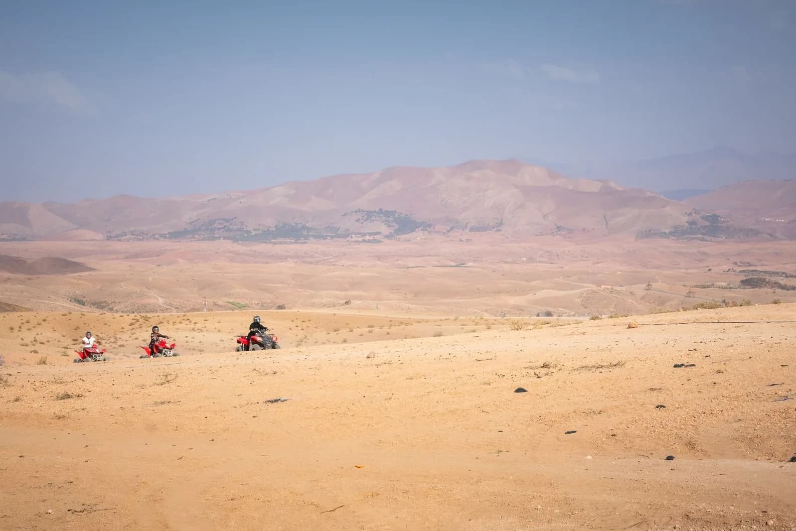 Groupe de quads en file sur un plateau rocailleux aride, avec des montagnes à l'horizon