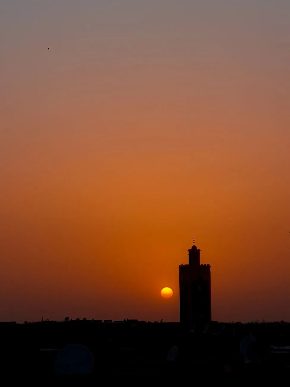 Soleil couchant derrière un minaret de Marrakech, vu depuis une terrasse en hauteur, ciel orange