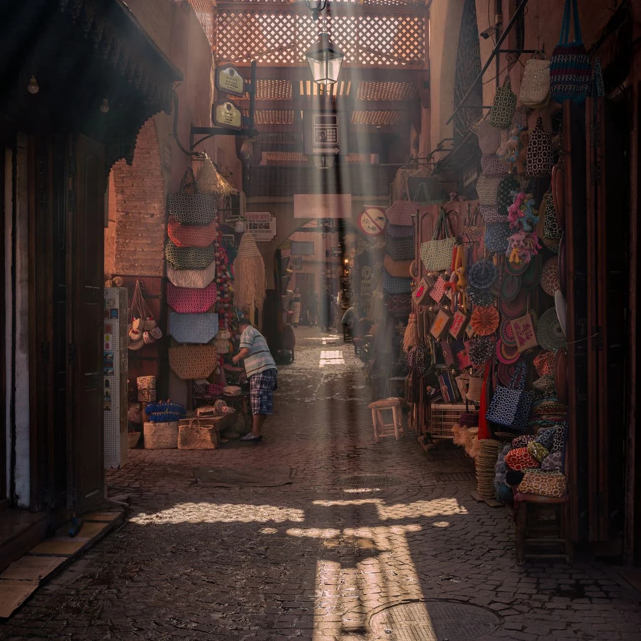 Ruelle ensoleillée des souks de la médina de Marrakech, échoppes d'artisanat coloré et rayons de lumière