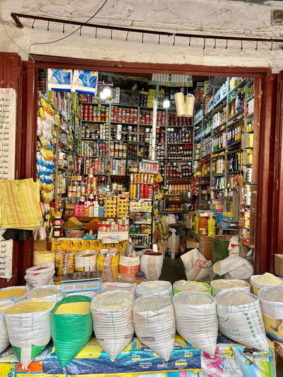 Épicerie de quartier marocaine aux étagères pleines, sacs de semoule et de farine en devanture