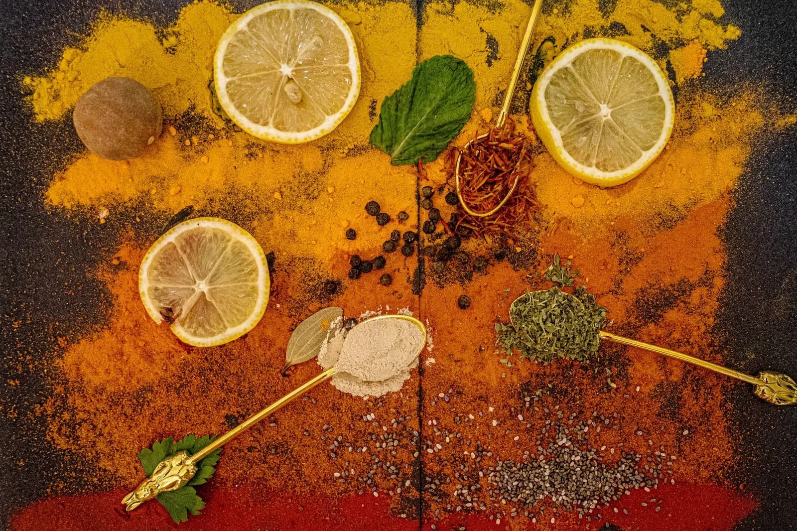 Épices en poudre, tranches de citron, safran, poivre et cuillères dorées posés à plat sur une table sombre