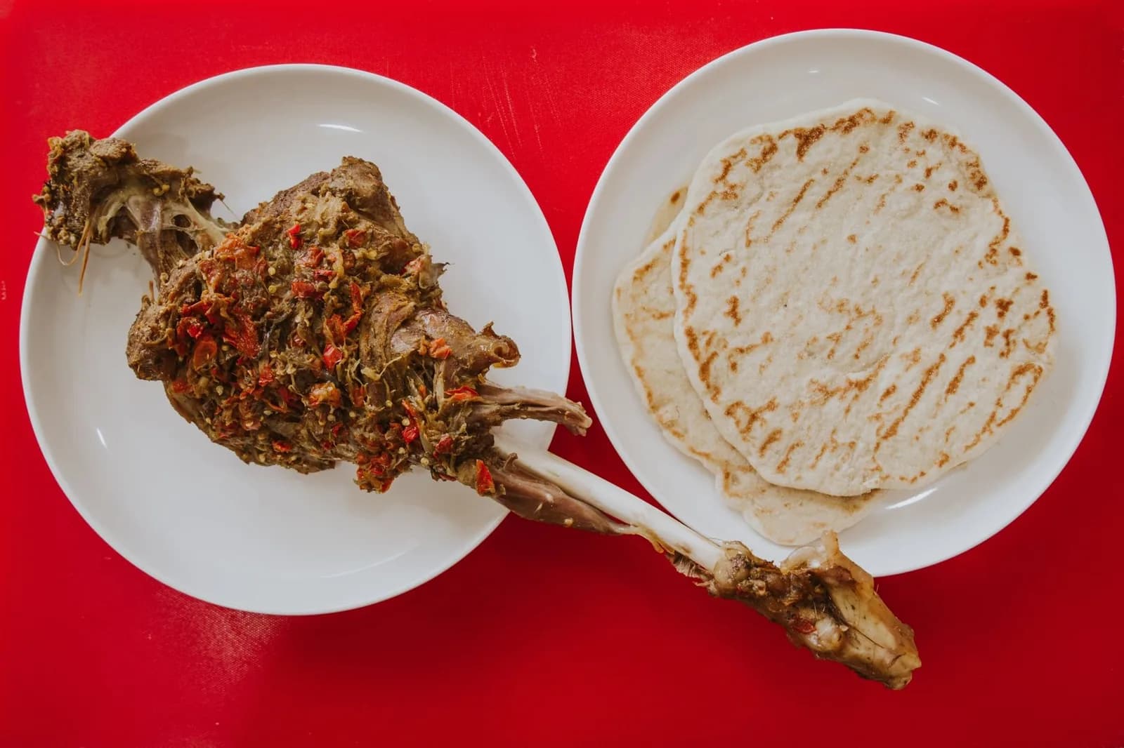 Viande braisée effilochée servie dans une assiette blanche, avec un pain plat grillé dans une seconde assiette