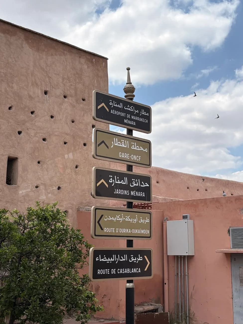 Panneau de signalisation bilingue à Marrakech indiquant la Gare ONCF et la route de Casablanca contre un mur ocre