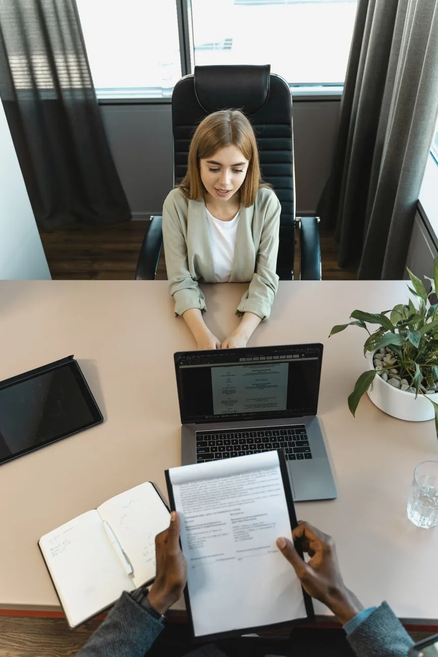 Entretien d'embauche vu de dessus : une candidate face à un recruteur qui tient son CV, ordinateur portable sur la table