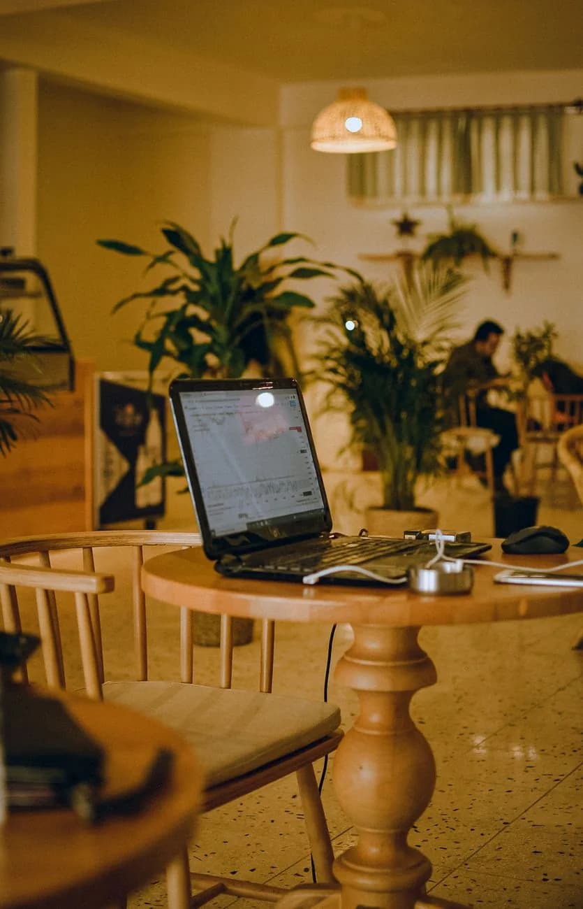Ordinateur portable ouvert sur une table en bois dans un café-coworking lumineux avec des plantes
