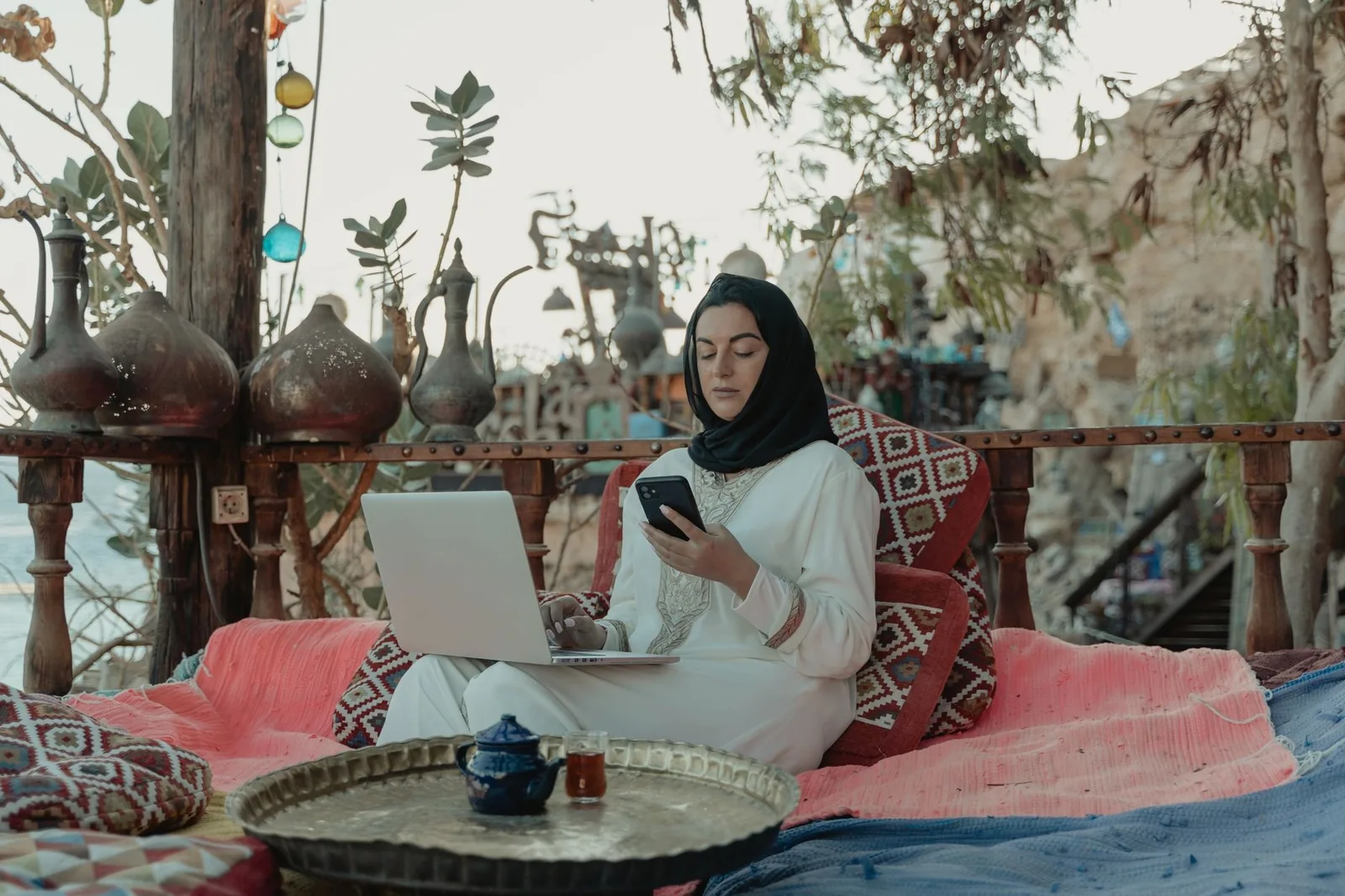 Femme travaillant sur un ordinateur portable sur une terrasse marocaine, à côté d'un plateau de thé à la menthe