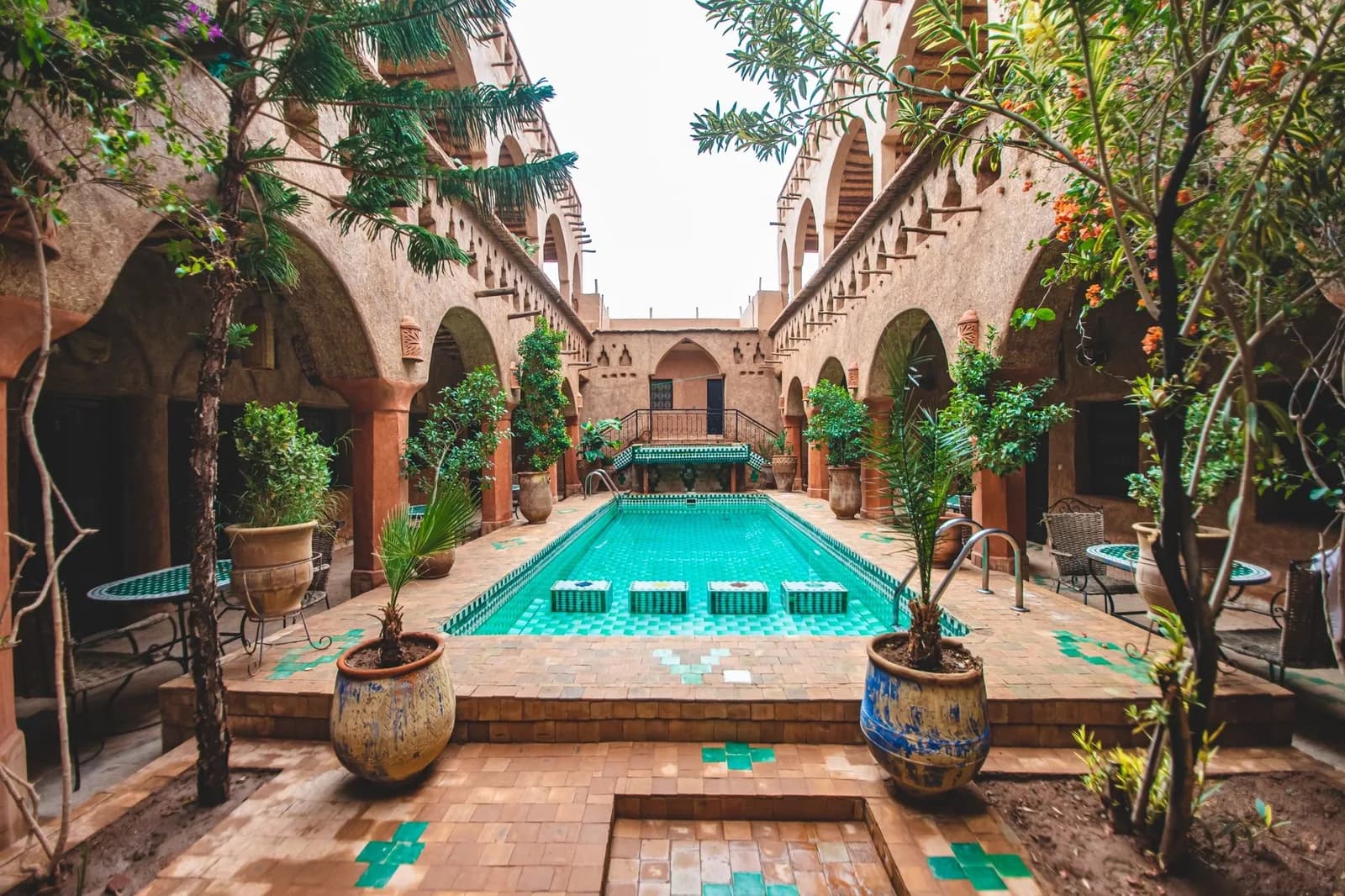 Patio d'un riad à Marrakech avec bassin turquoise, arcades ocre et plantes en pots